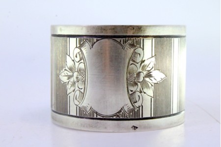 Argola de guardanapo em prata com bandas guilhochadas ao alto e motivos florais envolvendo cartela para monograma.